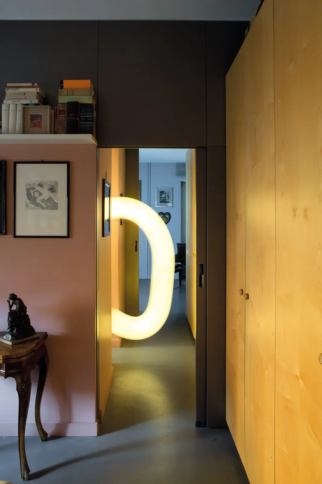 Casa Garbatella: corridoio con pareti rosa, armadiature in legno naturale e lampada scultorea