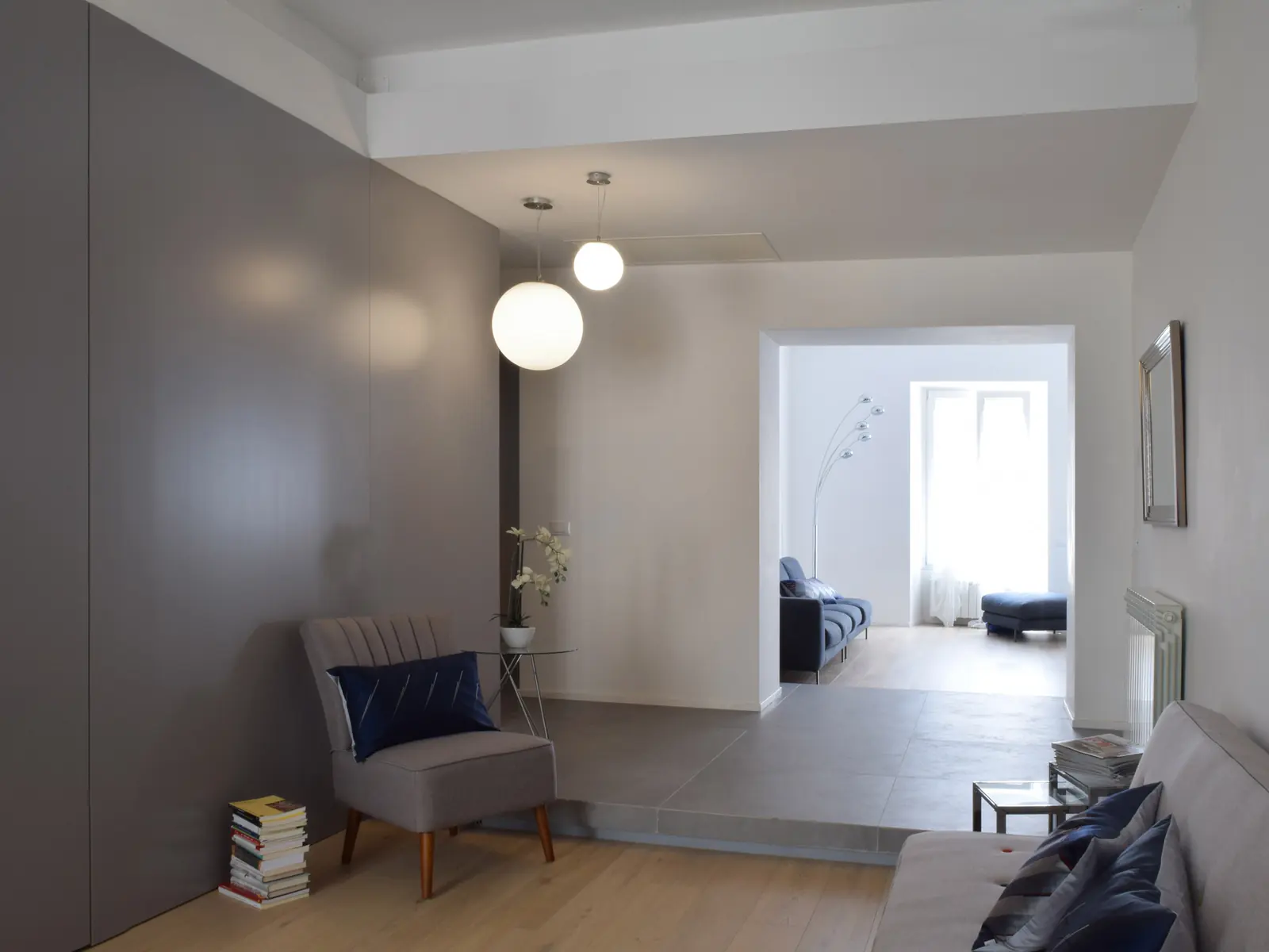 Living di Casa Scipioni con palette bianco-grigia, parquet e volumi su misura